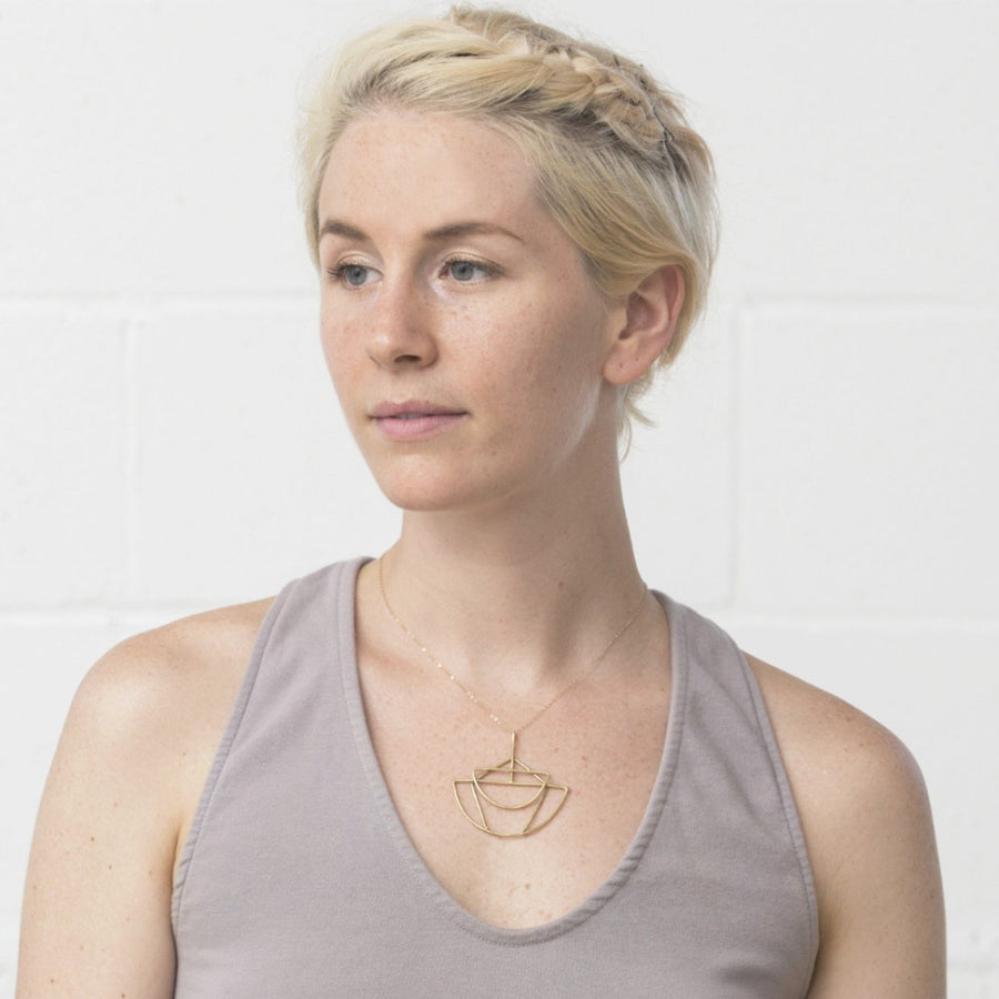 Model wears Sky Phaebl's Nembus bronze necklace. Interlaying cosmic symbols create a delicate yet eye catching pendant on gold-filled chain.