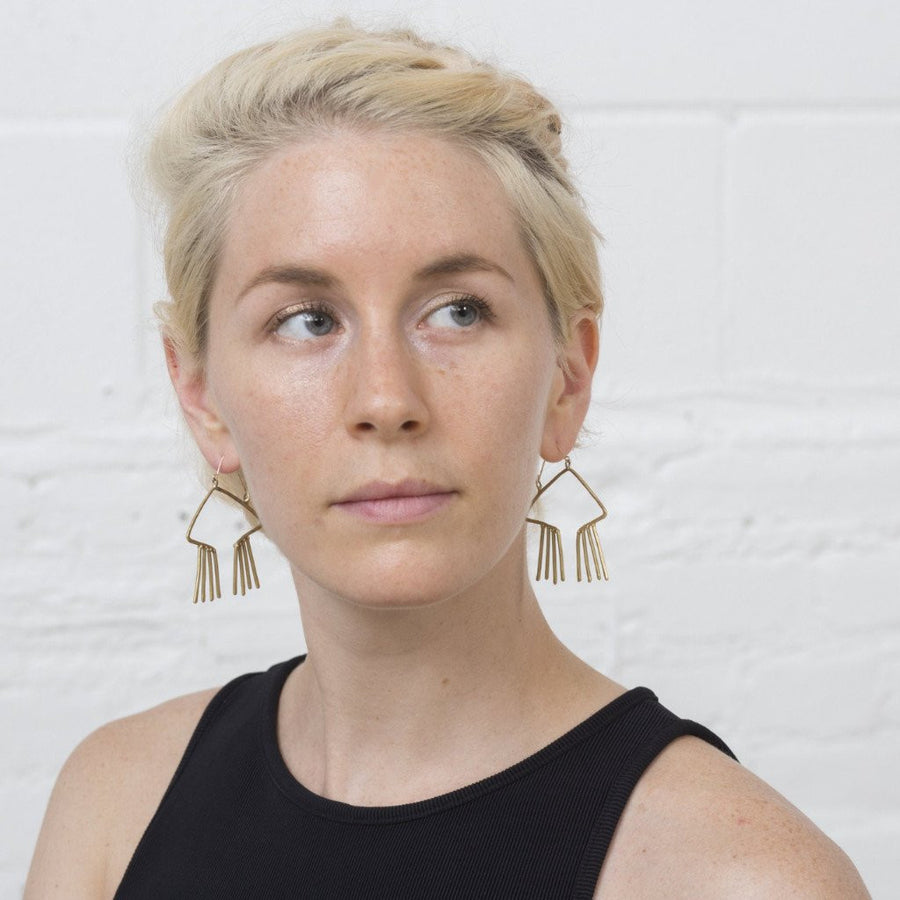 Model wears Sky Phaebl bronze and gold open, obtuse triangular earrings with hammer textured fixed fringe. 