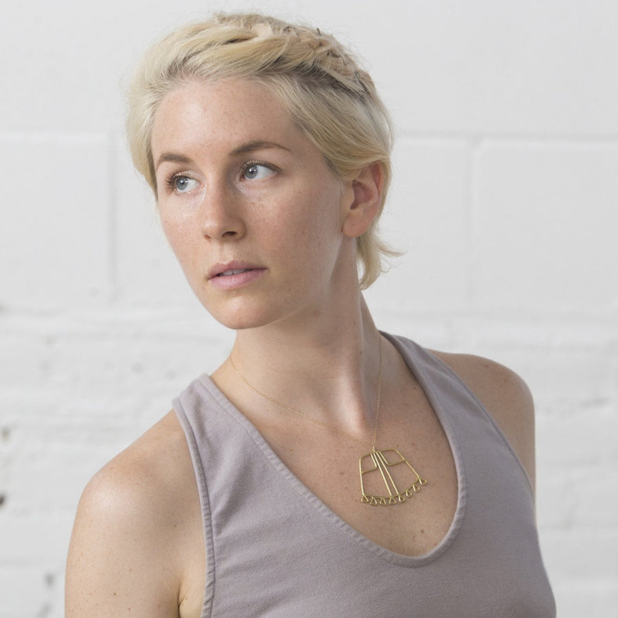 Model wears bronze Sky Phaebl curved trapezoid pendant lined with triangular fixed fringe and featuring linear filigree detail, on a fine gold-filled chain. Lays just below the clavicle.
