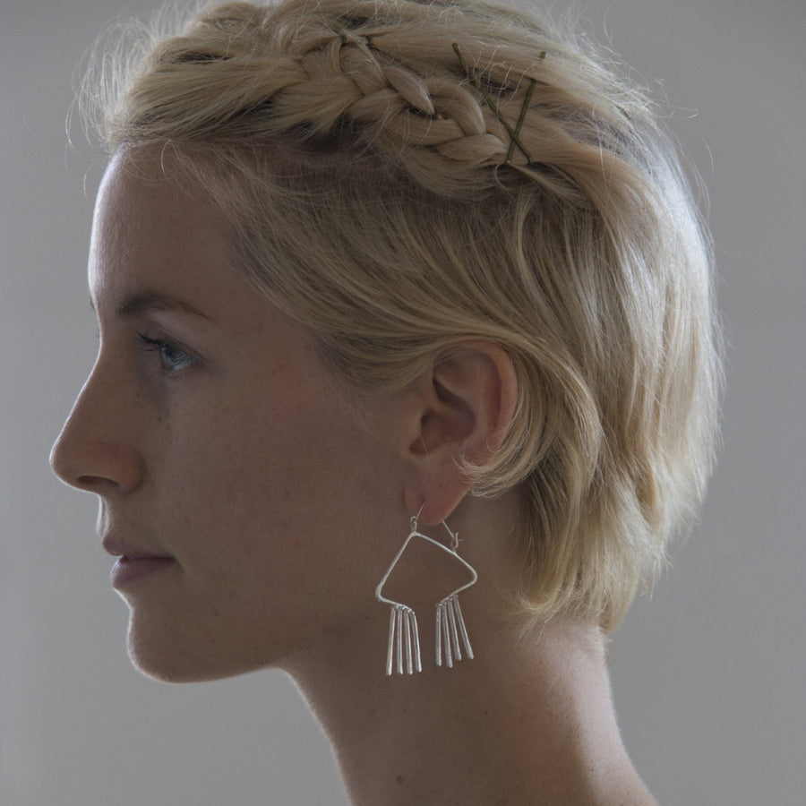 Model wears obtuse, open triangular earring with hammer textured fixed fringe. 